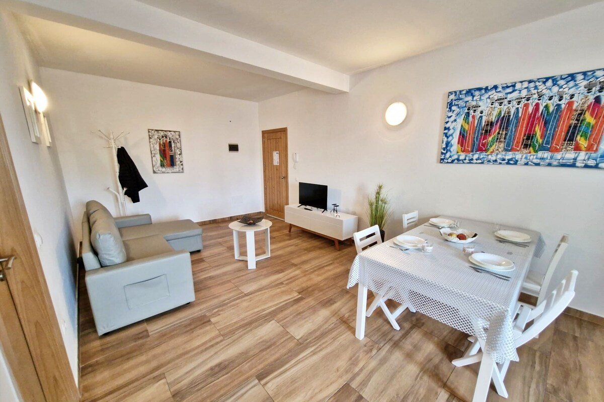 A modern living room with a sofa, a small round table, a dining table set for two, and a TV on a stand.