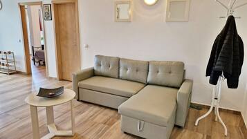 Ein modernes Wohnzimmer mit einem beigen Ecksofa, einem kleinen weißen Tisch und einem Garderobenhaken mit einer schwarzen Jacke.