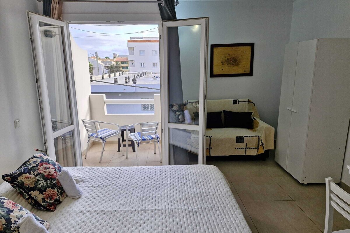 A bedroom with a bed, a balcony with chairs, a sofa, and a door leading outside.