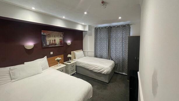 A hotel room with two beds, a nightstand, a lamp, a TV, and a painting on the wall. - The Sneyd Arms Hotel (Stoke-on-Trent)