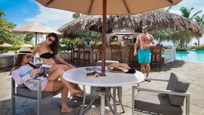 A poolside area with a round table, chairs, and a thatched umbrella. - Lifestyle Tropical Beach (Puerto Plata)
