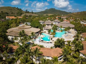 Ein Resort mit einem zentralen Schwimmbad, strohgedeckten Gebäuden und üppiger Vegetation.