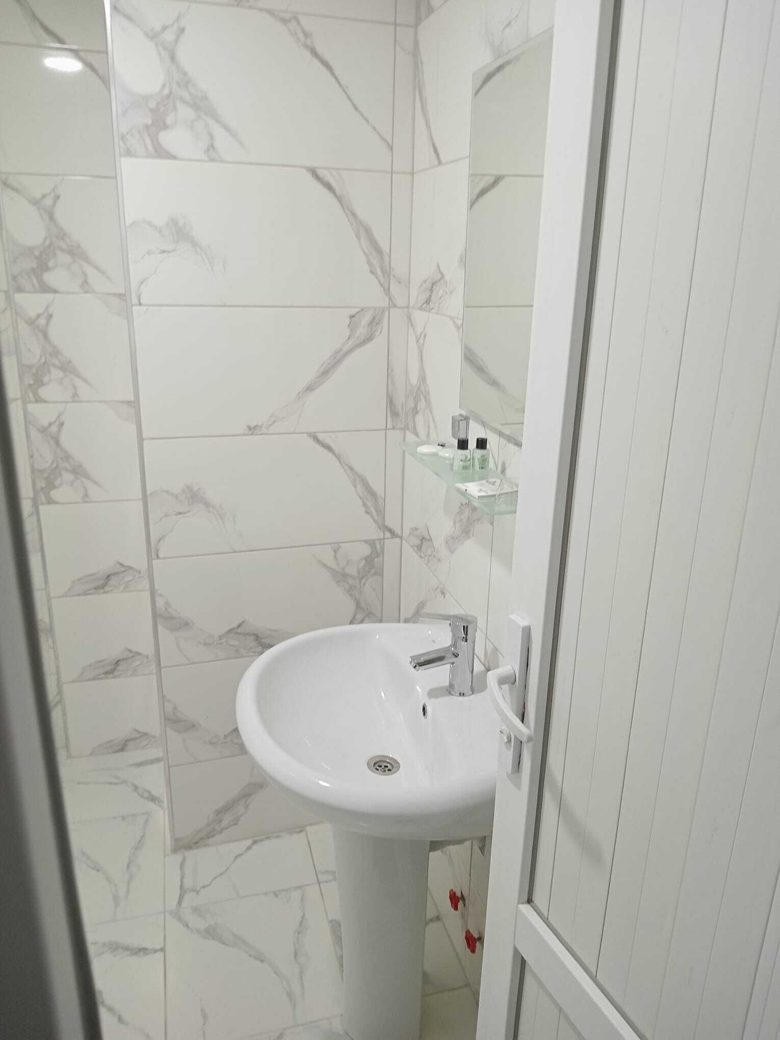 A bathroom with a white sink, marble-patterned walls, and a glass shelf with toiletries.