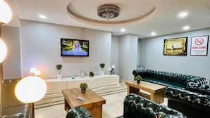 A modern living room with a black leather sofa, a wooden coffee table, a TV mounted on the wall, and a chandelier. - Lal Hotel (Istanbul)