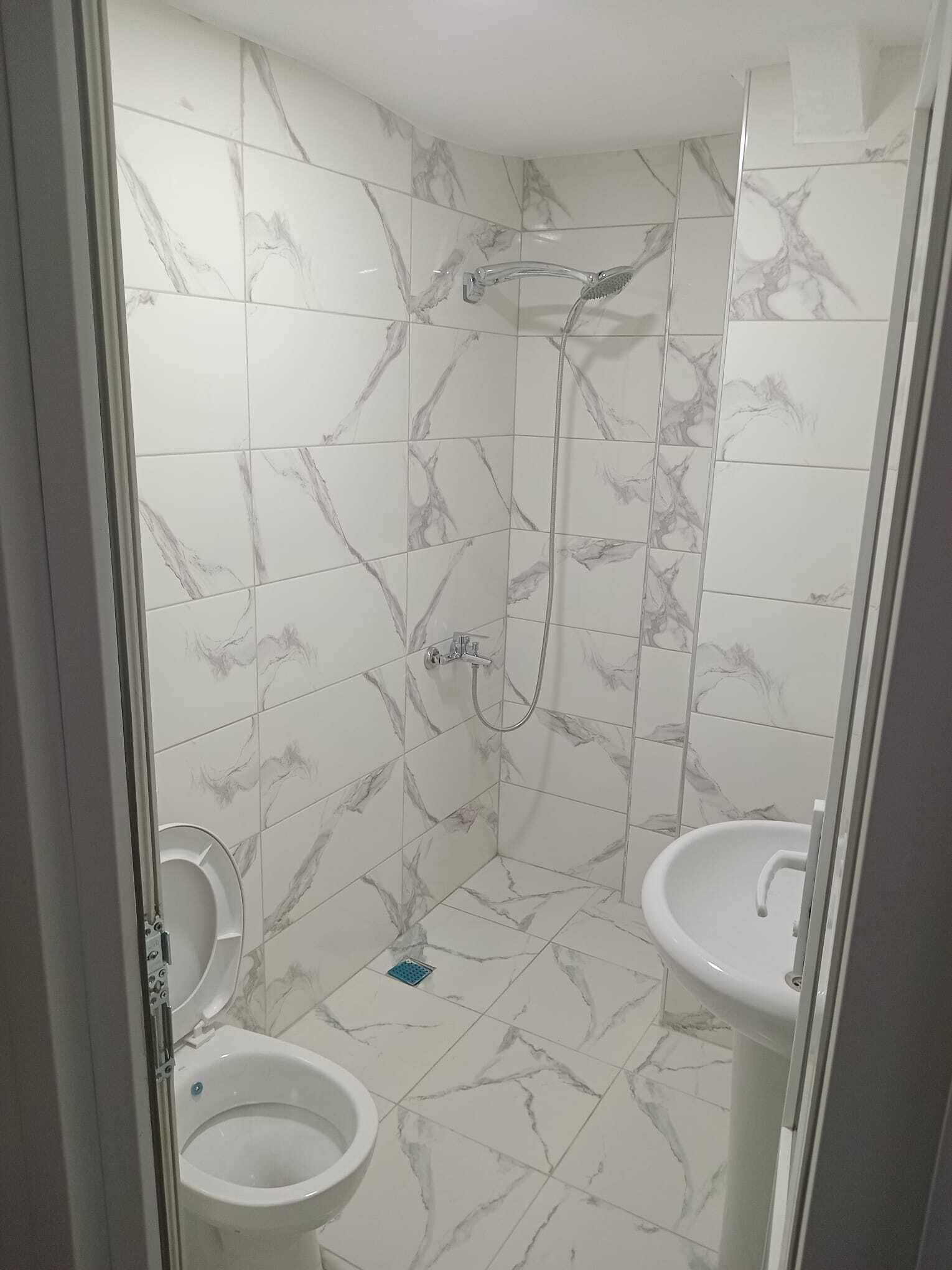 A bathroom with white marble tiles, a shower, and two sinks.