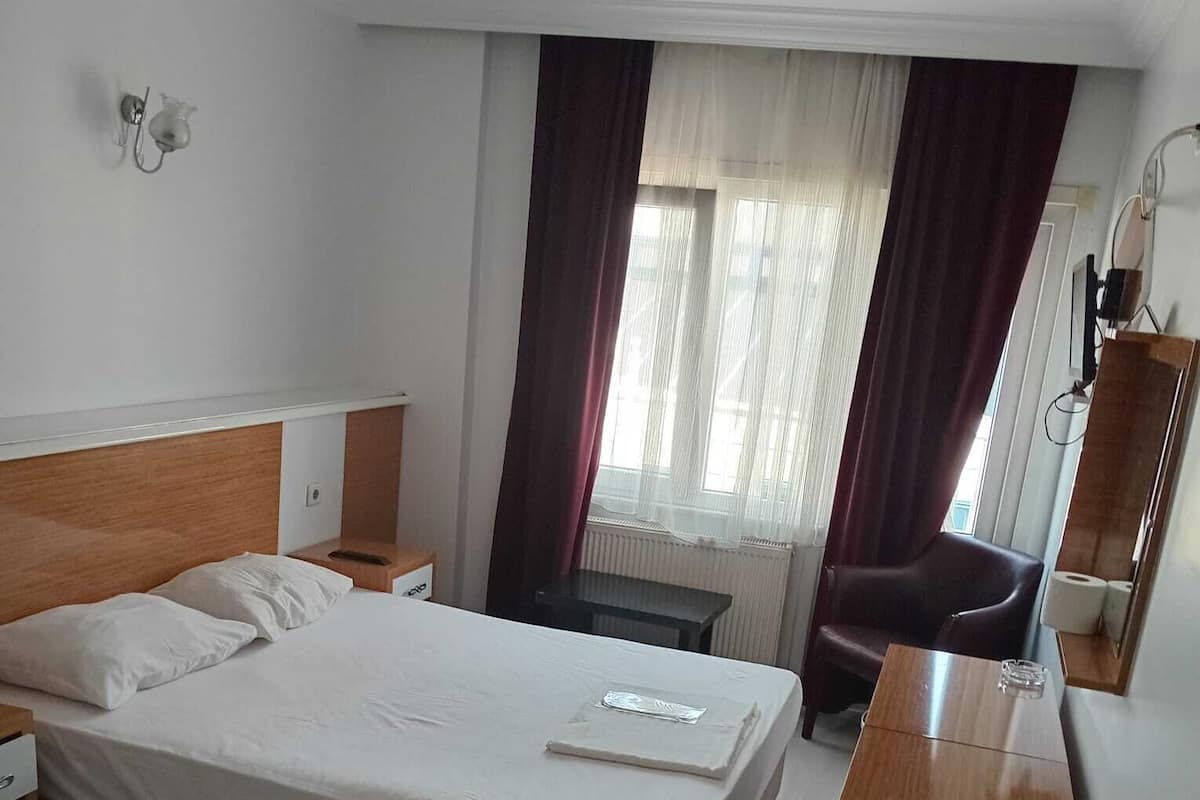 A hotel room with a bed, bedside table, chair, and a desk.