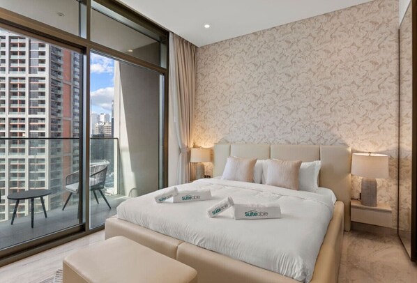 Una habitación de hotel moderna con una cama grande, un balcón con vistas a edificios altos y un papel tapiz estampado.