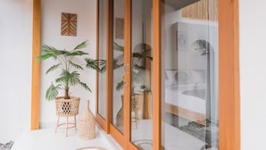 A modern room with a glass door, a bed, a small table with a plant, and a decorative wall piece. - Villa Niji - 3BR Villa with Pool Seseh (Munggu)