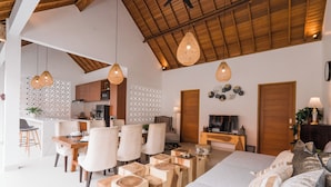 A modern living room with a sofa, dining area, kitchen, and wooden ceiling beams. - Villa Niji - 3BR Villa with Pool Seseh (Munggu)