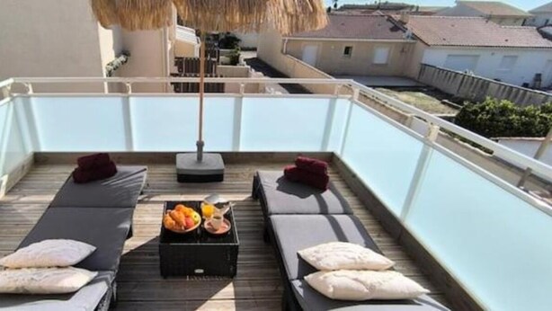 Terraza en la azotea con dos tumbonas, una mesa con frutas y una botella, y un paraguas de paja.