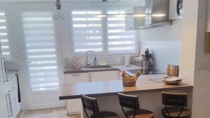 Una cocina moderna con una isla central, taburetes de bar y un ventanal con persianas.