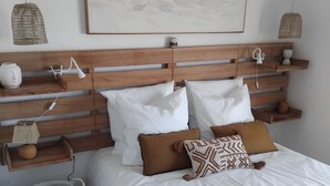 Un dormitorio ordenado con cabecera de madera, ropa de cama blanca y almohadones decorativos.