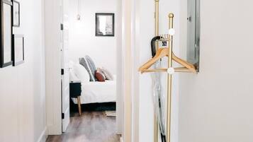Un pasillo con suelo de madera, un perchero con base blanca y una cama al fondo.