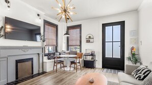 A modern living room with a fireplace, a dining area with a round table, and a large TV mounted on the wall.