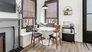 A modern kitchen with a round dining table, two wooden chairs, a black cabinet, and a black-framed window with a view.