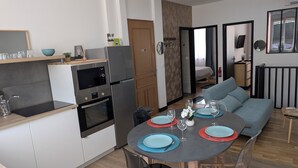 Une cuisine moderne dotée d’appareils électroménagers intégrés, un coin repas avec une table ronde et des chaises, et un salon avec un canapé et une vue sur l’extérieur.