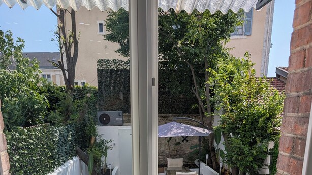 On aperçoit, à travers une porte vitrée, un jardin avec une piscine, des meubles d’extérieur et des plantes en pot.
