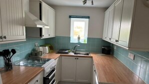 A compact kitchen with white cabinets, a sink, and a window. - Peaceful Cottage in Sound Healing Retreat (Cardigan)