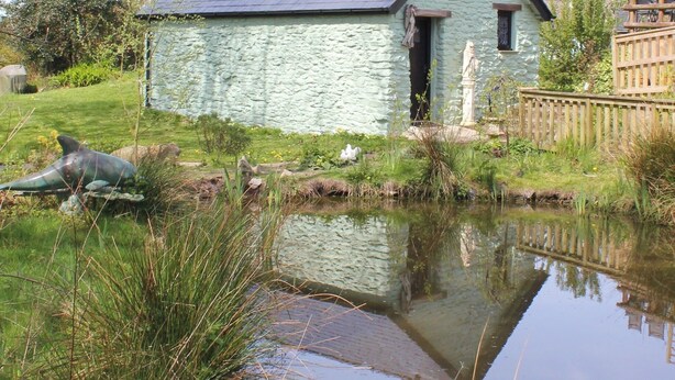 A stone cottage with a sloped roof, a small porch, and a pond in front. - Peaceful Cottage in Sound Healing Retreat (Cardigan)