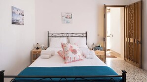 Een netjes opgemaakt bed met een blauwe sprei, witte kussens en een decoratief kussen. Twee nachtkastjes met lampen en een klein fotokader aan de muur.