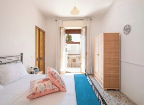 A bedroom with a bed, a wardrobe, a nightstand, and a view of the outside.