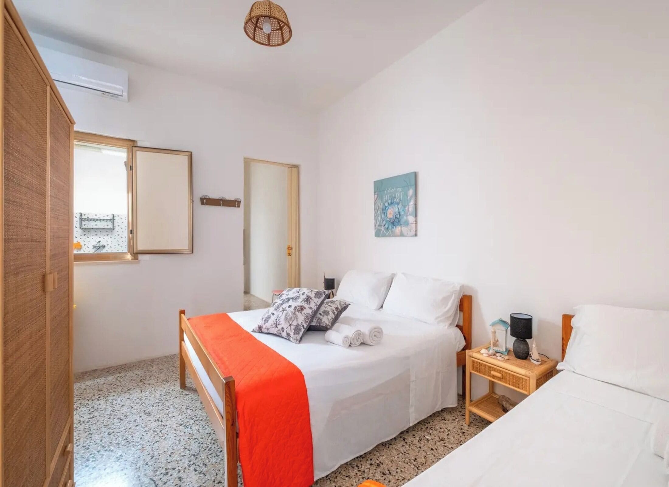 A bedroom with a bed, a nightstand, a wall-mounted air conditioner, a window, and a door.