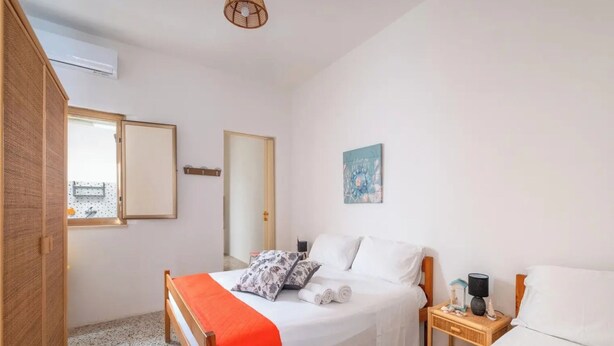 Een slaapkamer met een bed, nachtkastje, wandairconditioner, raam en deur.