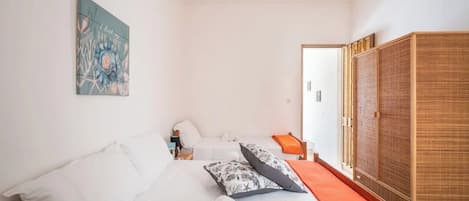 A bedroom with a bed, pillows, a rolled towel, a nightstand, a lamp, a painting, and a wardrobe.