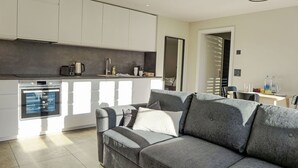 A modern kitchen with white cabinets, a built-in oven, and a dining area with a table and chairs.