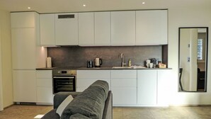 A modern kitchen with white cabinets, a built-in oven, and a countertop with a kettle and coffee maker.