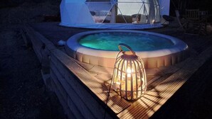 A geodesic dome structure with a hot tub and a lantern on a wooden deck.
