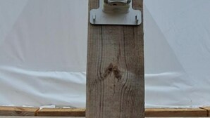 A wooden post with a white object attached to it, possibly a mailbox or a sign, against a backdrop of a white wall and a wooden structure.