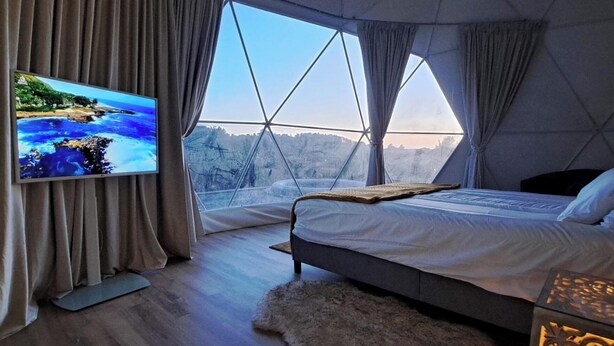 A modern bedroom with a large window, a bed, a TV, and a fur rug.