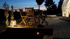 An outdoor deck with wooden chairs and a table, a lantern, and a tent-like structure.