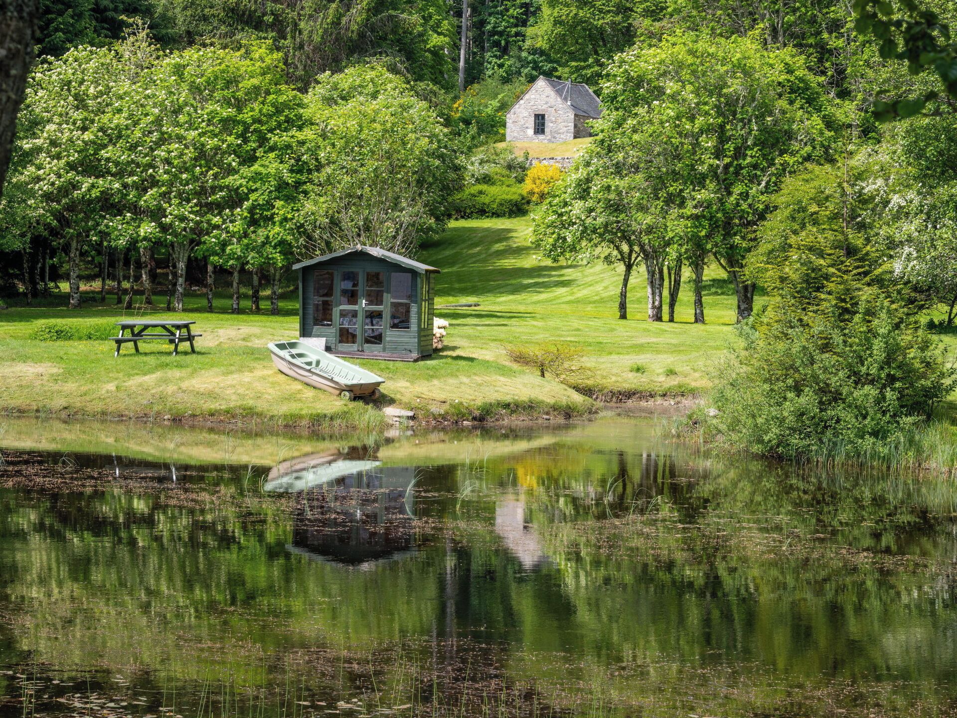 Uma cabana à beira do lago com um cais, rodeada por vegetação exuberante e árvores.