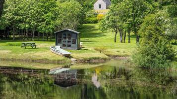 Uma cabana à beira do lago com um cais, rodeada por vegetação exuberante e árvores.