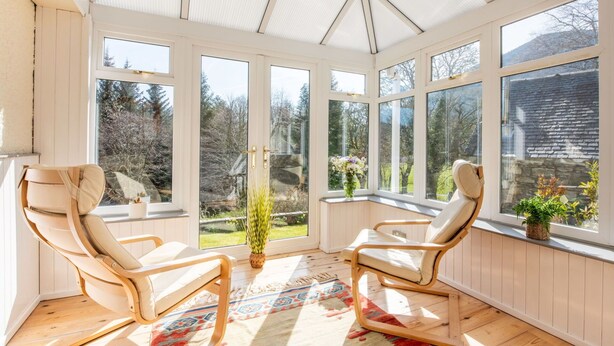 A sunroom with two wooden chairs, large windows, and a view of a garden. - Beautiful private villa for 8 guests with WIFI, TV, patio and panoramic view (Invermoriston)
