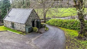 A stone cottage with a sloped roof, a small porch, and a gravel driveway leading to a green lawn. - Beautiful private villa for 8 guests with WIFI, TV, patio and panoramic view (Invermoriston)