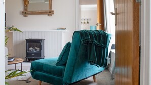A teal velvet armchair with a throw blanket, a wood-burning stove, and a mirror on the wall.