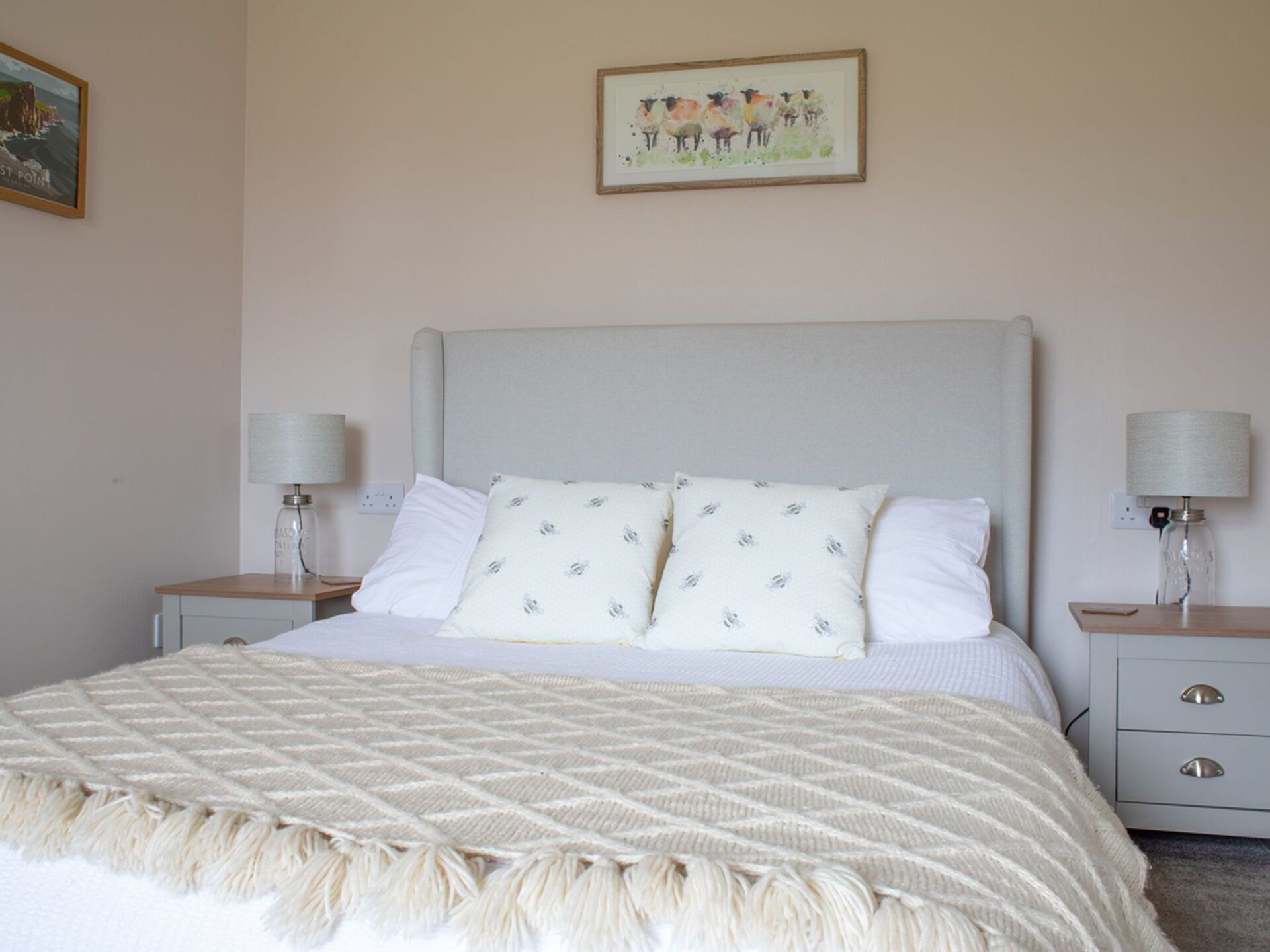 Cama bem arrumada com manta acolchoada e duas almofadas, com mesas de cabeceira com luminárias, em um quarto simples e limpo.