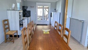 A dining area with a wooden table and chairs, a kitchen with a stove and refrigerator, and a door leading outside.