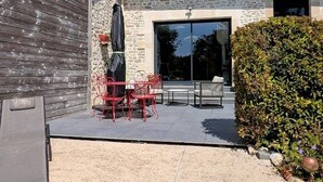 Eine Terrasse mit roten Metallstühlen und einem Tisch, eine Steinmauer und eine große Glastür zu einem Innenraum.