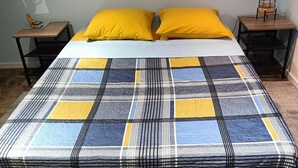 Ein Bett mit kariertem Überwurf, zwei gelbe Kissen und zwei Nachttische mit Lampen.