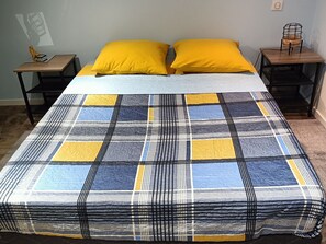 Un lit avec une couvre-lit à carreaux, deux oreillers jaunes et deux tables de chevet avec des lampes.