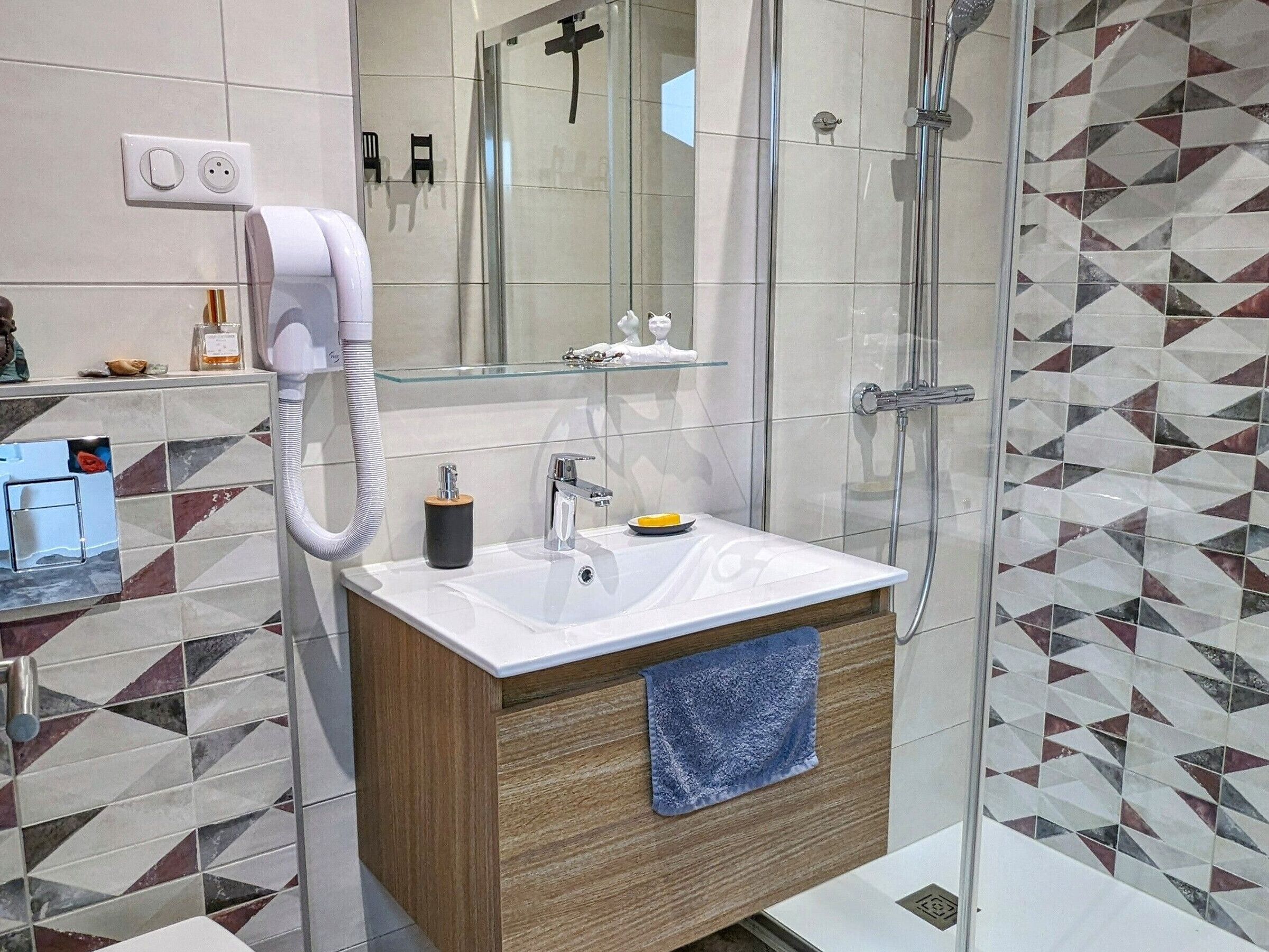 Une salle de bain moderne avec une douche à l’italienne en verre, un lavabo blanc avec un meuble-vasque en bois et un miroir au-dessus du lavabo.