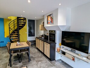 A modern kitchen with a built-in oven, a large flat-screen TV, and a wooden dining table with chairs. - Renovated apartment with sunny terrace and parking in Pierrefitte-sur-Aire (Pierrefitte-sur-Aire)