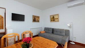 A living room with a grey sofa, a wooden dining table with chairs, a TV mounted on the wall, and a radiator. - Lovely apartment for 4 guests with A/C, WIFI, TV and terrace (Trogir)