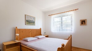 A wooden bed with a headboard, a bedside table with a lamp, a window with sheer curtains, and a painting on the wall. - Lovely apartment for 4 guests with A/C, WIFI, TV and terrace (Trogir)