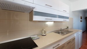 A modern kitchen with white cabinets, a black induction cooktop, a stainless steel sink, and a built-in range hood. - Lovely apartment for 4 guests with A/C, WIFI, TV and terrace (Trogir)
