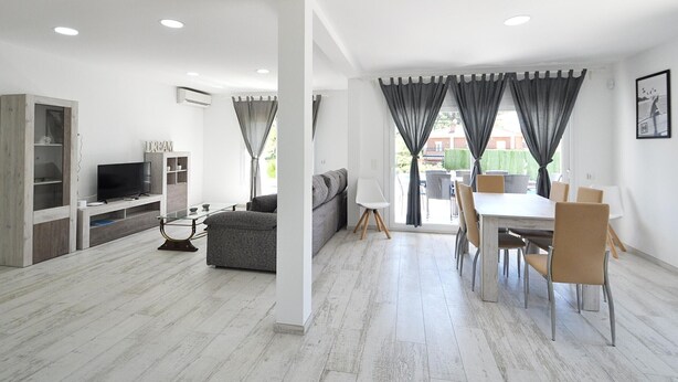 Una sala moderna con sofá, televisor y comedor con sillas y mesa.